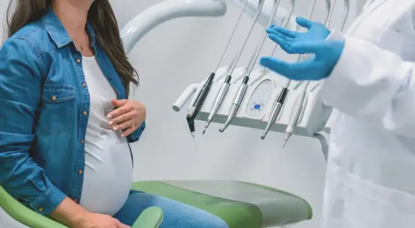 Ciężarna kobieta w gabinecie stomatologicznym, omawiająca leczenie kanałowe.