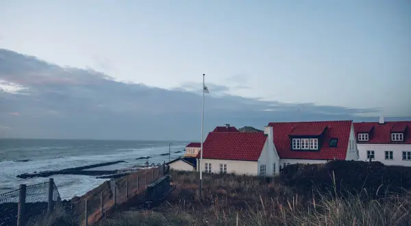Vackra vita hus med röda tak vid havet, perfekt för en **weekendresa Danmark**. Gräs och staket i förgrunden.