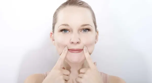 Une femme pratique le yoga du visage, ses doigts pressant ses joues pour un sourire accentué.