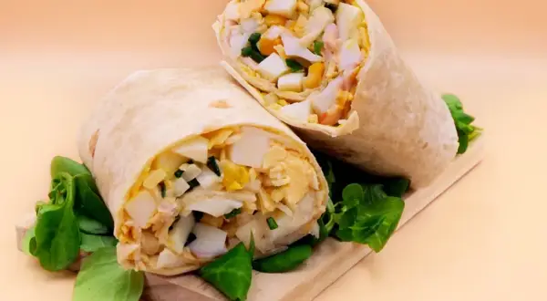 Pyszna tortilla z jajkiem, warzywami i kurczakiem, podana na desce z zieloną sałatą. Idealna na szybki lunch.