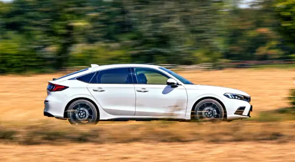 Biały Honda Civic 2025 pędzi przez suche pole, zostawiając za sobą smugi kurzu i rozmazane drzewa.