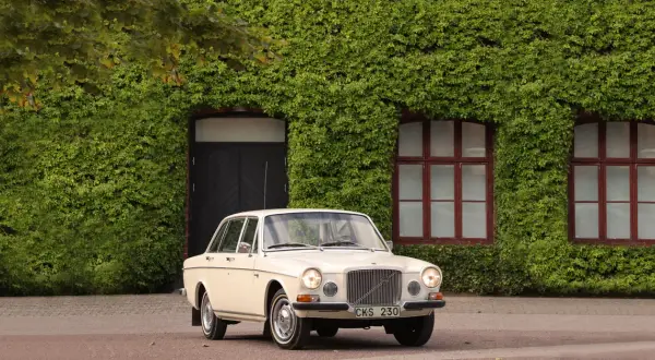 En klassisk Volvo 164 från 1973 parkerad framför en vackert klätterväxttäckt byggnad.