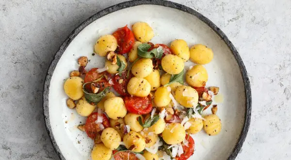 Pyszne gnocchi z sosem pomidorowym, listkami szałwii i orzechami laskowymi, posypane parmezanem.