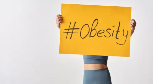 Osoba trzymająca tabliczkę z napisem #Obesity. Problem otyłości w Polsce staje się coraz poważniejszy.