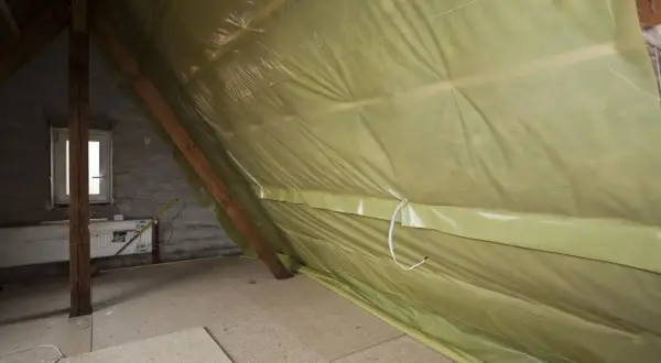 Podczas ocieplania poddasza, odpowiednia folia pod wełnę mineralną na strop zapobiega zawilgoceniu. Widoczna żółta folia paroprzepuszczalna chroni izolację.