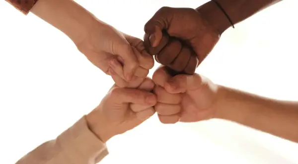 Vier Fäuste stoßen zusammen, ein Symbol für **diversity in der pflege**. Hände verschiedener Hautfarben vereinen sich in einem Zeichen der Solidarität und des Zusammenhalts.