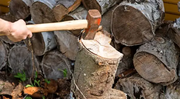 Holz spalten mit Axt. Auch wenn es nass wird, darf Brennholz so gelagert werden, bis es trocken ist.