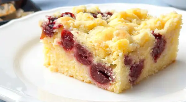 Ein Stück saftiger Kirschstreuselkuchen vom Blech auf einem weißen Teller, mit vielen Kirschen und knusprigen Streuseln.