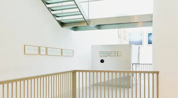 Interno moderno con scale in vetro e metallo. Opere di Christian Martinelli appese alle pareti bianche.