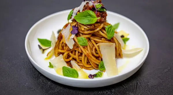 Pyszne spaghetti alla norma z sosem pomidorowym, bakłażanem, bazylią i parmezanem, podane na białym talerzu.