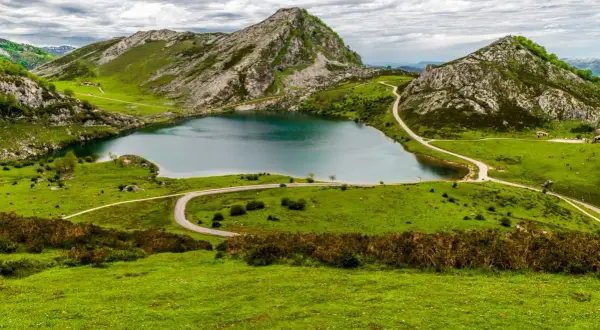 Un lago sereno rodeado de verdes colinas y picos rocosos, un paisaje idílico para ver Picos de Europa.