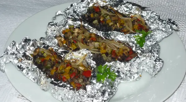 Kaszanka z grilla z cebulą i warzywami, zapieczona w folii aluminiowej, podana na białym talerzu.