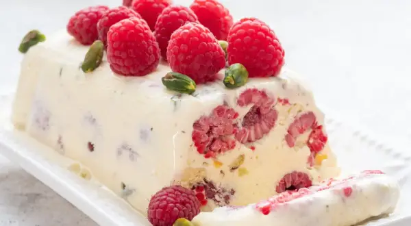 Pyszne lody z ciasta z malinami i pistacjami, ozdobione świeżymi owocami. Idealny deser na gorące dni.