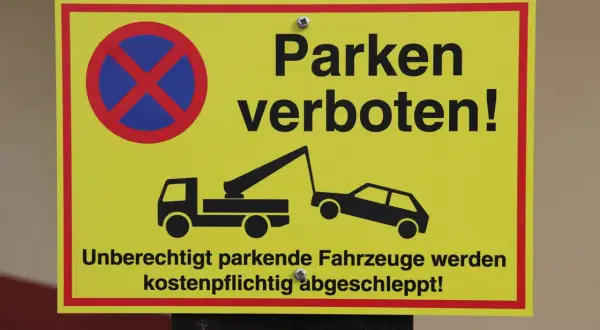 Gelbes Schild: Parken verboten! Ein Abschleppwagen holt ein schlecht geparktes Auto ab. Unberechtigt parkende Fahrzeuge werden kostenpflichtig abgeschleppt!
