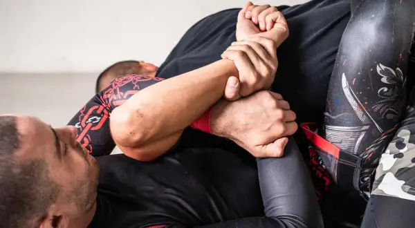 Två män brottas på en matta. En av dem har en omoplata bjj-position.