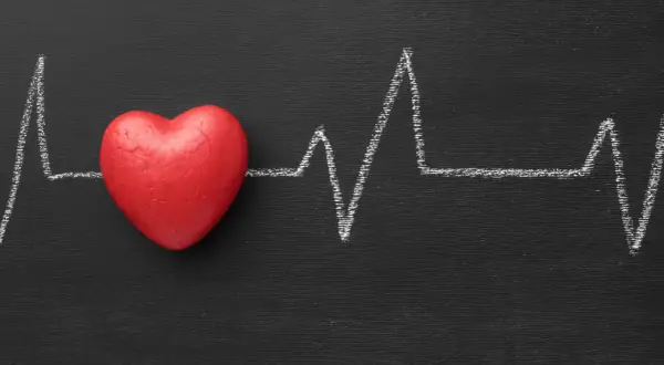 Cuore rosso su lavagna nera con tracciato ECG. Un simbolo di cosa fa alzare la pressione.