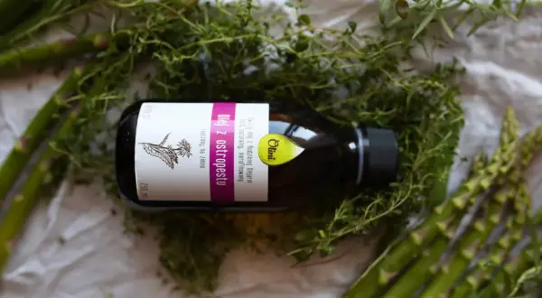 Olej z ostropestu na twarz efekty? Butelka oleju z ostropestu wśród ziół i szparagów. Naturalna pielęgnacja dla Twojej skóry.