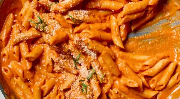 Penne alla vodka w kremowym, pomarańczowym sosie, posypane parmezanem i świeżą bazylią.