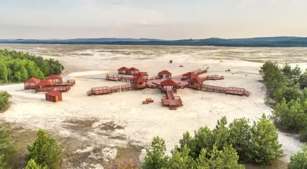 Pustynia Błędowska z widokiem na architekturę przypominającą różę wiatrów, z drewnianymi altanami i pomostami na piaszczystym terenie.