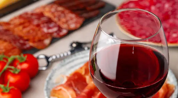 Glas Rotwein neben Aufschnitt und Tomaten. Ein Fest für Genießer, das den Unterschied Portwein Sherry erahnen lässt.