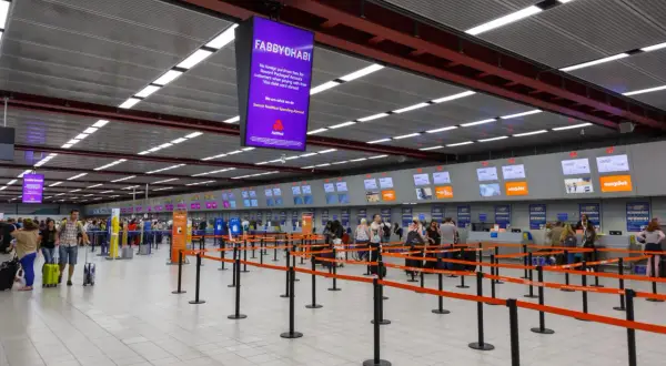 Kasa odpraw na lotnisku Londyn Luton. Pasażerowie z bagażami czekają w kolejce do stanowisk linii lotniczych easyJet.