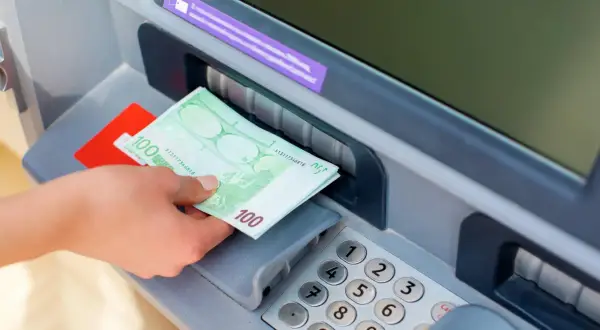 Ręka odbiera banknoty 100 euro z bankomatu PKO.