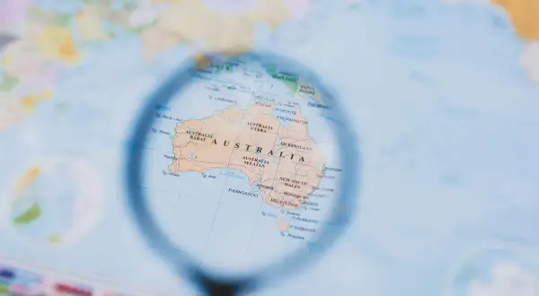 Mapa świata z lupą powiększającą Australię. Planowanie, kiedy są wakacje w Australii, to świetny pomysł na podróż!
