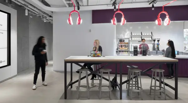 Inside Spotify Studios NYC, people gather around a communal table, with iconic headphone lights overhead.