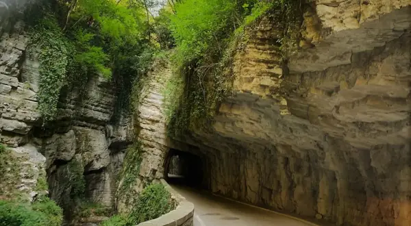 Strada della forra in moto, un percorso suggestivo tra rocce scolpite e vegetazione lussureggiante, con un tunnel che si apre nel verde.