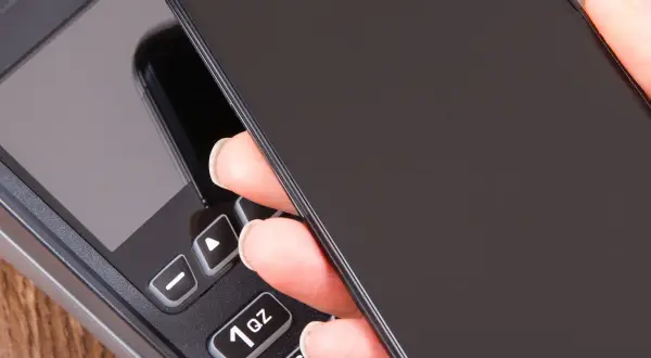 Zbliżenie na dłoń trzymającą telefon nad terminalem płatniczym. Szybki sposób, jak doladowac telefon Play.