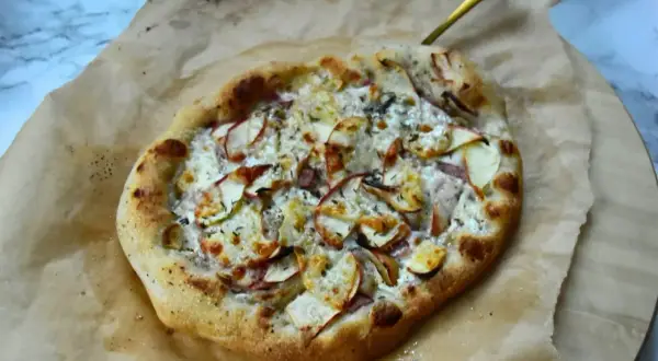Pyszna pizza bianca z jabłkami i serem, podana na papierze do pieczenia.
