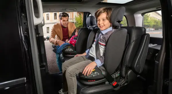 Padre sistema un bambino su un seggiolino auto, rispettando la normativa seggiolini auto. Un altro bambino è già seduto.
