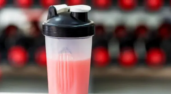 Przezroczysty shaker z różowym napojem na tle czerwonych kółek.