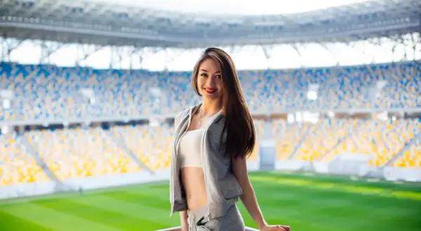 Uśmiechnięta dziewczyna w sportowym stroju na tle stadionu. Idealny przykład, jak się ubrać na mecz, by czuć się komfortowo i stylowo.