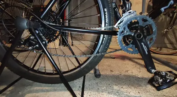 Widok tylnego koła i korby roweru. Pokazuje mechanizm przerzutek i łańcuch, który można naciągnąć, aby rower działał płynnie.