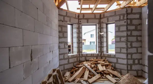 Interno di una casa in costruzione con muri in blocchi di cemento, tetto in legno e cumuli di legname. Forse un caso di abuso edilizio prescrizione.
