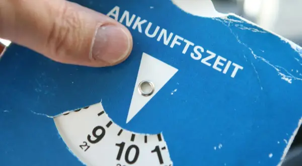 Ein Finger dreht die Scheibe einer Parkscheibe, um die Ankunftszeit einzustellen. So funktioniert eine Parkuhr: Zeit einstellen, auslegen, fertig.