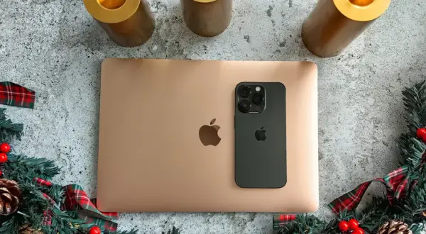 Złoty MacBook i czarny iPhone na tle świątecznych dekoracji. Idealny zestaw do pracy i rozrywki z macOS.