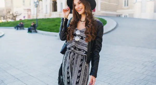 Uśmiechnięta dziewczyna w kapeluszu i skórzanej kurtce, prezentująca styl glamour ubrania.