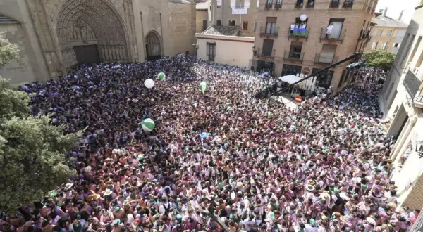 Multitud celebra en la plaza de Huesca, con globos verdes y blancos flotando. La fiesta prelaurentis inunda las calles.