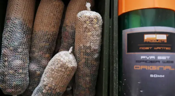 Kilka woreczków z zanętą w siatce PVA, obok zielony pojemnik z pomarańczową nakrętką, na którym widnieje napis "PVA SET SPIDER WEB ORIGINAL".