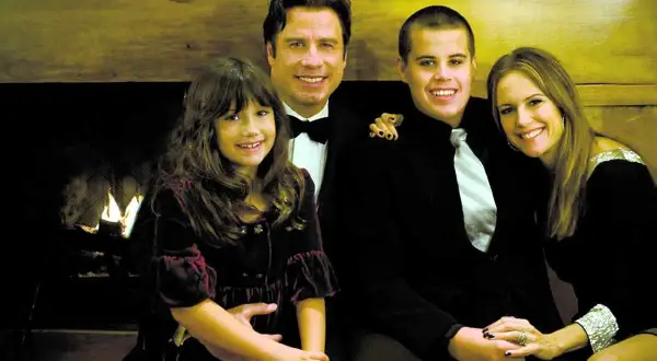 John Travolta med familjen, inklusive sonen Jett, poserar glatt framför en öppen spis.