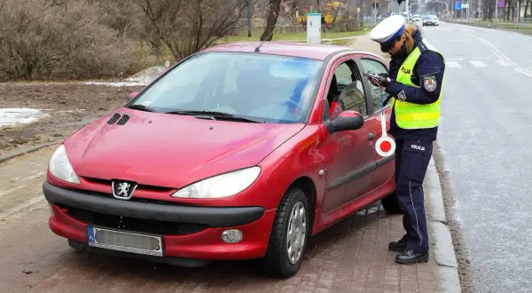 Policjantka kontroluje dokumenty kierowcy czerwonego Peugeota, grozi mu utrata prawa jazdy za punkty.