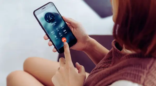 Kobieta trzyma telefon, na ekranie połączenie od nieznanego numeru. Zastanawiasz się, jak sprawdzić, czy telefon jest na podsłuchu?