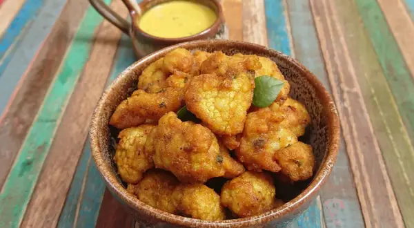 Beignets de choux-fleurs dorés et croustillants, servis dans un bol en terre cuite avec une sauce jaune crémeuse. Parfaits pour un apéritif savoureux.
