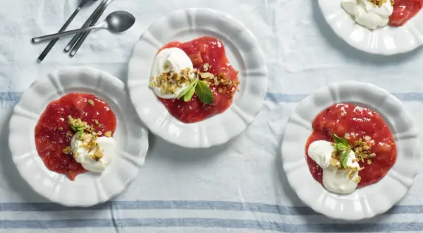 Tre vita skålar med rabarberkompott kardemumma, toppad med grädde och nötter. En härlig dessert.