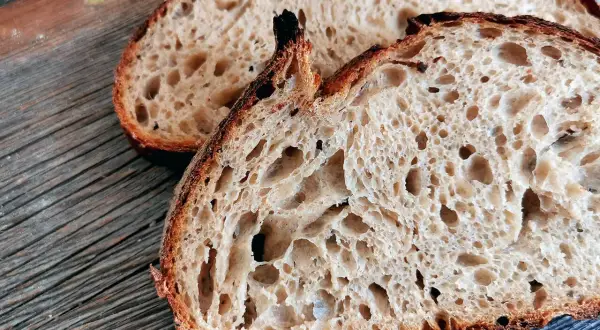 Zwei Scheiben rustikales Sauerteigbrot mit knuspriger Kruste und luftiger Krume liegen auf einem Holzbrett. Ein gesundes Frühstück!