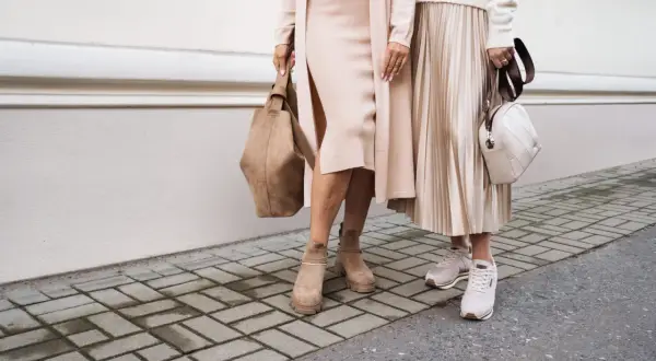 Dwie kobiety w beżowych sukienkach i kardiganach, jedna w zamszowych botkach, druga w sneakersach. Stylowe buty do beżowej sukienki.