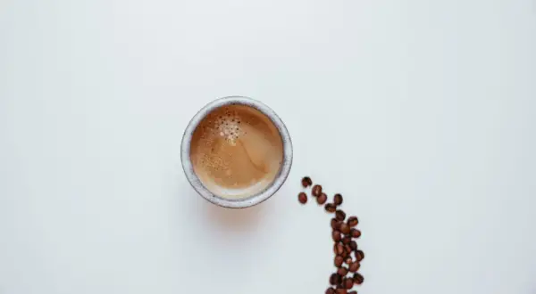 Un caffè pregiato, con la sua crema invitante, accanto a chicchi tostati su sfondo bianco.