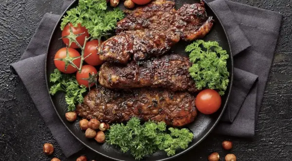 Saftiges Putenschnitzel braten, garniert mit Kirschtomaten, Petersilie und Haselnüssen auf schwarzem Teller.